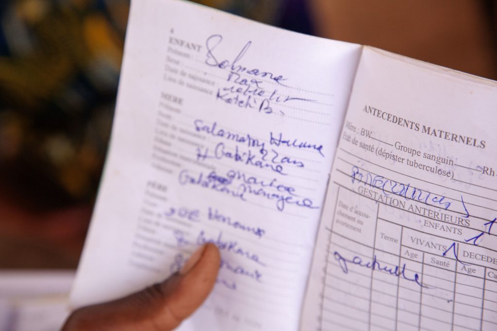 أم تحمل سجل التحصين، والذي يتم إعطاؤه لكل طفل عند الولادة حتى يتمكن العاملون الصحيون من ضمان حصول الطفل على اللقاحات اللازمة في الوقت المناسب، خلال حملة التطعيم ضد شلل الأطفال في قرية توتو، منطقة دوسو، النيجر، الخميس 14 أبريل 2016. يعيش غالبية السكان في النيجر بعيدًا عن المرافق الصحية. يتم تنظيم برامج التوعية الصحية من أجل توفير الخدمات الصحية للأشخاص الذين يعيشون في المناطق النائية. يسافر العاملون الصحيون إلى منطقة محددة في تاريخ محدد لإجراء التطعيمات وفحوصات ما قبل الولادة، مع إبلاغ السكان الموجودين داخل دائرة نصف قطرها 17 كيلومترًا مسبقًا. وقد أدت هذه الاستراتيجية إلى زيادة تغطية التطعيم في المنطقة، والتي تبلغ الآن 98%. ولم تعد النيجر مصابة بفيروس شلل الأطفال، وفقًا للمبادرة العالمية للقضاء على شلل الأطفال، ولكنها لا تزال معرضة لخطر تفشي المرض. إن اكتشاف فيروس شلل الأطفال البري من النوع 1 (WPV1) في عام 2016 في شمال شرق نيجيريا يعني أن المنطقة بأكملها معرضة للخطر حاليًا. وأعلنت النيجر، إلى جانب بلدان أخرى في منطقة بحيرة تشاد الفرعية، أن تفشي المرض يمثل حالة طوارئ إقليمية للصحة العامة وتقوم بتنفيذ استجابة إقليمية للفاشية، بالتنسيق مع البلدان المجاورة. وينتشر شلل الأطفال من خلال الاتصال الشخصي. عندما يصاب الطفل بفيروس شلل الأطفال البري، يدخل الفيروس الجسم عن طريق الفم ويتكاثر في الأمعاء. ومن ثم يتم طرحه في البيئة من خلال البراز حيث يمكن أن ينتشر بسرعة عبر المجتمع، وخاصة في حالات سوء النظافة والصرف الصحي. وإذا تم تحصين عدد كاف من الأطفال بشكل كامل ضد شلل الأطفال، فلن يتمكن الفيروس من العثور على الأطفال المعرضين للإصابة بالعدوى، ويموت. وفي النيجر، يعيش غالبية السكان بعيداً عن المرافق الصحية. ومن أجل توفير الخدمات الصحية للأشخاص الذين يعيشون في المناطق النائية، يتم تنظيم برامج التوعية الصحية. يسافر العاملون الصحيون إلى القرى المحددة لإجراء التطعيمات وفحوصات ما قبل الولادة. فيلا اليونيسف/UN026553/باري