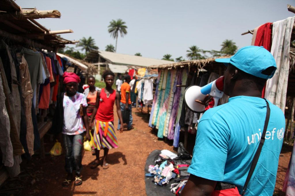 On 24 April 2014, a UNICEF outreach worker uses the opportunity to convince marketers that Ebola is in Liberia on a market day in Voinjama, Lofa County, where groups of people gather to sell their products,.
In April 2014 in Liberia, UNICEF workers share information on the symptoms of Ebola virus disease (EVD) and best practices to help prevent its spread in Lofa County, including posters bearing information on and illustrations of such practices. As of 27 July 2014, a total of 1,323 cases, including 729 deaths, had been attributed to EVD in the four West African countries of Guinea, Liberia, Nigeria and Sierra Leone. Liberia has borne 329 of these cases (100 confirmed, 128 probable and 101 suspected), including 156 deaths. UNICEF/UNI167510/Jallanzo