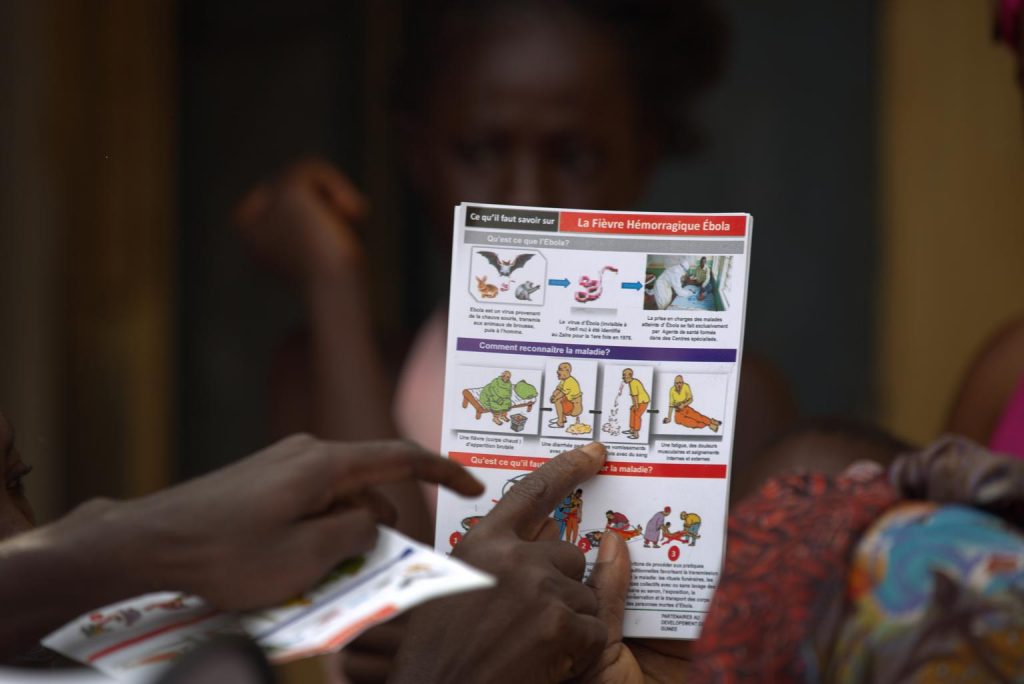 Le 20 août 2014, en Guinée, un employé de l'UNICEF distribue des dépliants d'information sur la maladie à virus Ebola (MVE) et les meilleures pratiques pour aider à prévenir sa propagation, dans le quartier de Matam à Conakry, la capitale. En plus d'enseigner aux résidents des informations essentielles sur la MVE et de distribuer des dépliants, l'agent distribue également du savon et du chlore dans la communauté. Au 18 août, un total de 2 473 cas de MVE (cas confirmés en laboratoire, probables et suspects) ainsi que 1 350 décès avaient été signalés en Guinée, au Libéria, au Nigeria et en Sierra Leone. La Guinée a enregistré 396 de ces décès. UNICEF/UNI169293/La Rose