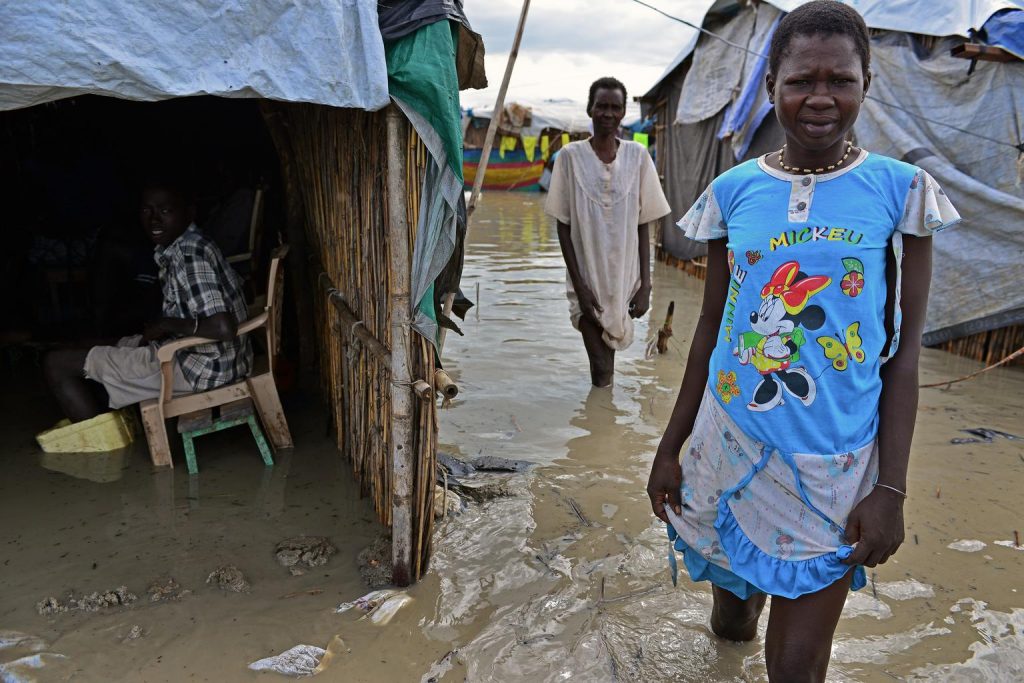 On 23 August, (left-right) two displaced women making their way through floodwaters pass a boy sitting in a flooded shelter, at the Bentiu Protection of Civilians (POC) site, located on the United Nations peacekeeping mission in South Sudan (UNMISS) base near the city of Bentiu, capital of Unity State, following heavy rains. Shelters in several areas at the PoC site remain largely flooded, exacerbating living conditions for the sites approximately 40,000 displaced and increasing the risk of waterborne disease. An estimated 1.3 million people have been displaced since resurgent conflict erupted in mid-December 2013. More than 695,000 of the displaced are children. About 442,600 people have also sought refuge in neighbouring countries. UNICEF has appealed for US $151.8 million to cover emergency responses across the vital areas of nutrition; health; water, sanitation and hygiene (WASH); protection; education; multi-sector refugee response; and cholera response. By 19 August, 52 per cent remained unfunded. UNICEF/UNI169359/Nesbitt