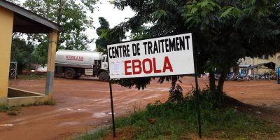 On 17 October 2014 in Guinea, a sign reads, in French, CENTRE DE TRAITEMENT EBOLA, meaning Ebola treatment centre, outside an Ebola virus disease (EVD) case management centre run by Médecins Sans Frontières in the town of Guéckédou, in Guéckédou Prefecture, Nzérékoré Region. The town is near the village of Meliandou, where, through retrospective case-finding, 2-year-old Emile Ouamouno was found to be the first person to have contracted EVD in what would ultimately become the largest-ever outbreak of the disease. Emile passed away in December 2013, followed shortly thereafter by his 4-year-old sister, Philomène, and then his mother, both of whom also contracted the virus. By late October in West Africa, Guinea, as well as Liberia and Sierra Leone, continued to experience widespread and intense EVD transmission. Following successful response to an initial case or cases imported from a country with widespread and intense transmission, Senegal and Nigeria were declared free of EVD on 17 and 19 October, respectively. Mali reported its first confirmed case of EVD on 23 October; contact monitoring and tracing are still ongoing. UNICEF/UNI173876/Beukes