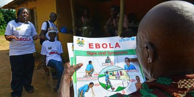On 19 November 2014, Sanfa Koroma, a 14 year-old Ebola survivor, seated centre alongside social mobiliser Agnes Ngele, speaks with village elders during a mobilization session in the village of Gbonjiema, in Moyamba district in the Southern Province of Sierra Leone.
Sanfa Koroma, 14-years-old, was studying in a Koranic school in the village of Gbonjiema, two hours walk away from his small home town of Palewahun. He became infected along with another boy, and was taken to the district capital, Bo. The news came back from several separate health officials that he had died. A traditional funeral ceremony was organised; mourners cooked and shared a meal, and some food was set aside to feed Sanfas spirit on its journey to the next life. Only Sanfa wasnt dead. Slowly, some rumours began to reach the community that Sanfa was alive. The entire village turned out to welcome the returnee. UNICEF provided support to the family reunification, assuring the presence of a social service officer from the Ministry of Social Welfare, Gender and Childrens Affairs, delivering a Reunification and Family Tracing (FTR) kit and helping to arrange the distribution of food rations by WFP. Sanfa returned home with a 25kg bag of rice, bags of beans, ½ gallon of palm oil and the essentials to start life again from scratch. Back in the village Gbonjiema, UNICEF are carrying out social mobilization activities to spread awareness about Ebola and how to avoid it. The visiting team from UNICEFs partner, ACF, start the sensitisation event by greeting the chief and working up the ambience with traditional songs and dances. Sanfa Koroma starts speaking in Mende, one of the local languages in Sierra Leone. Every member of the village listens attentively. His voice sounds secure and clear. Just looking at him, they can see that Ebola isnt a death sentence. People in the Ebola treatment centre gave me food and drinks and they encouraged me. I knew that I was going to get better, UNICEF/UNI176936/Nesbitt