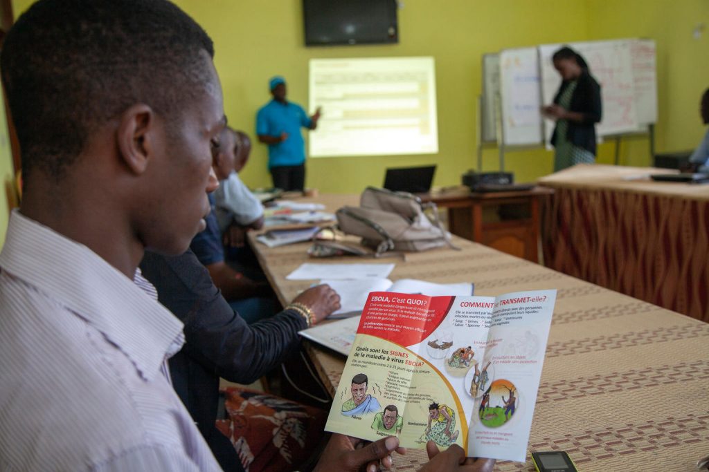 On 9 August 2018, a humanitarian partner reads an Ebola prevention pamphlet during a UNICEF training in prevention messaging in Ebola-hit North Kivu, DRC. As at 8 August 2018, UNICEF briefed 60 community leaders in Mabalako health zone and 581 community members in Beni health zone on Ebola prevention messages as well as distributed 200 posters and 300 Ebola prevention pamphlets. Mass communication on Ebola prevention messages is being integrated into activities of local churches and local radio stations with 241 churches having received Ebola prevention messages and 79 local journalists being briefed.
Following the 1 August 2018 announcement by the Government of the Democratic Republic of the Congo (DRC) of a new Ebola Virus Disease (EVD) outbreak in North Kivu, UNICEF has mobilized its teams to help contain the spread of the disease and protect children. The impact of an outbreak on children can be far reaching. It’s known from earlier outbreaks in the DRC as well as in West Africa that children can be affected in various ways. Children can themselves be infected by the disease, but the impact goes beyond; it impacts their families and communities as children can lose their parents, care-givers and teachers. Access to basic services such as health care and education can become severely compromised. Also, children who are infected or whose relatives are, face stigmatization and social exclusion.
The Congolese Government has activated its response plan and called its partners, including UNICEF, to participate in the response. UNICEF has deployed a team to Beni for the response, including health specialists, communication specialists and a water, sanitation and hygiene specialist from the Ebola-response team in the Province of Equateur. Health, water, sanitation and hygiene and communication supplies have been sent to the affected areas including 300 laser thermometers to monitor the health conditions of people in the affected region and 2,000 kg of chlorine UNICEF/UN0228764/Naftalin