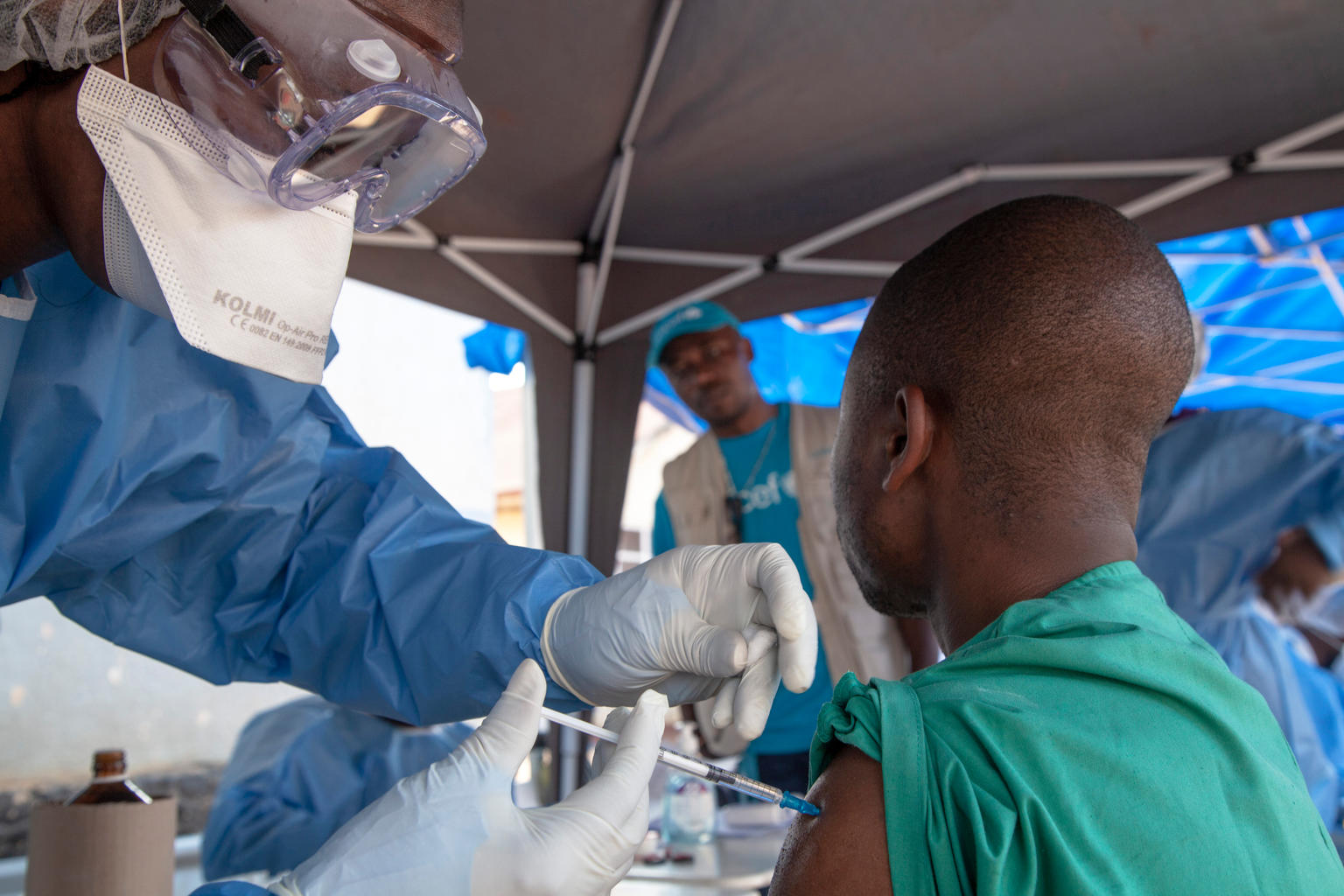 On 10 August 2018, an Ebola vaccination team member (left) prepares to administer the Ebola vaccine in Beni, North Kivu, the Democratic Republic of the Congo (DRC).
Following the 1 August 2018 announcement by the Government of the Democratic Republic of the Congo (DRC) of a new Ebola Virus Disease (EVD) outbreak in North Kivu, UNICEF has mobilized its teams to help contain the spread of the disease and protect children. The impact of an outbreak on children can be far reaching. It’s known from earlier outbreaks in the DRC as well as in West Africa that children can be affected in various ways. Children can themselves be infected by the disease, but the impact goes beyond; it impacts their families and communities as children can lose their parents, care-givers and teachers. Access to basic services such as health care and education can become severely compromised. Also, children who are infected or whose relatives are, face stigmatization and social exclusion.
The Congolese Government has activated its response plan and called its partners, including UNICEF, to participate in the response. UNICEF has deployed a team to Beni for the response, including health specialists, communication specialists and a water, sanitation and hygiene specialist from the Ebola-response team in the Province of Equateur. Health, water, sanitation and hygiene and communication supplies have been sent to the affected areas including 300 laser thermometers to monitor the health conditions of people in the affected region and 2,000 kg of chlorine to treat water to help contain the spread of the disease. As at 14 August 2018, UNICEF has installed 35 chlorination points, as well as handwashing units in 45 public places and in health facilities in the affected areas of Beni and Mangina in North Kivu. UNICEF has supported the distribution of prevention posters and leaflets, and worked with communities, in public places and with local radio stations to promote safe hygiene and sanitation UNICEF/Naftalin