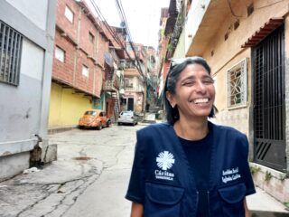Smiling woman wearing a blue Caritas jacket standing in street setting